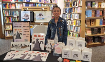 Amelia, who received early intervention after a bilateral sensorineural hearing loss diagnosis, smiling for a photo in front of a table with her books, at an author reading inside Barnes & Noble. 