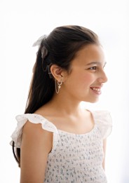 Amelia, who received early intervention after a bilateral sensorineural hearing loss diagnosis, pictured from the side, wearing a white dress, and smiling, with her cochlear implant visible over her ear. 