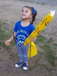Amelia, who received early intervention after a bilateral sensorineural hearing loss diagnosis, smiling while looking up at the sky, and holding a Cochlear branded Thunder stick.
