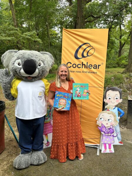 Katie smiling with Cochlear's Kaci the Koala holding the Might Mila books. 